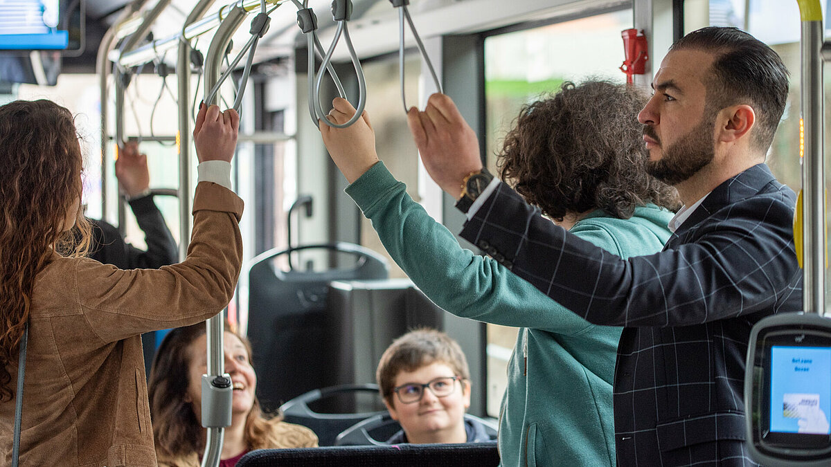 Three passengers are holding on to the handles of the bus