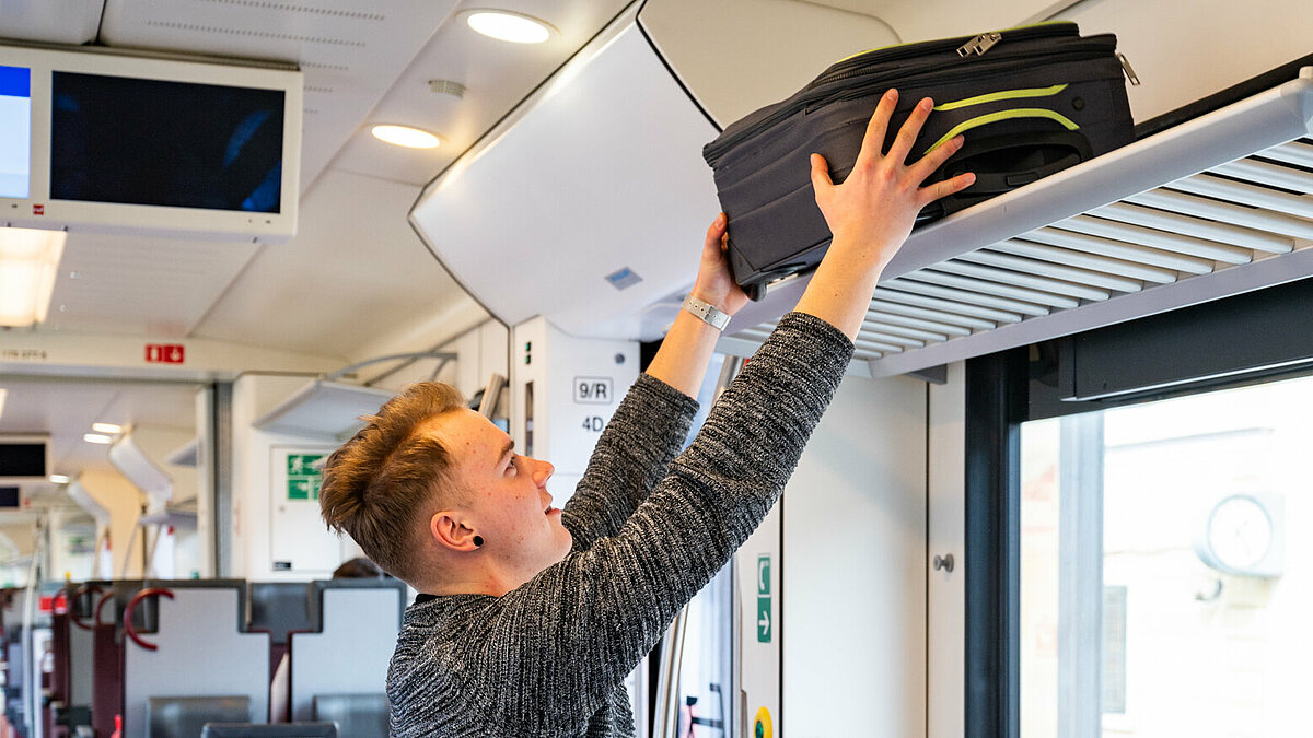 A passenger is loading a suitcase on the luggage rack on the train