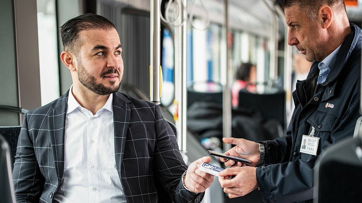 A ticket inspector is checking the ticket of a sitting passenger