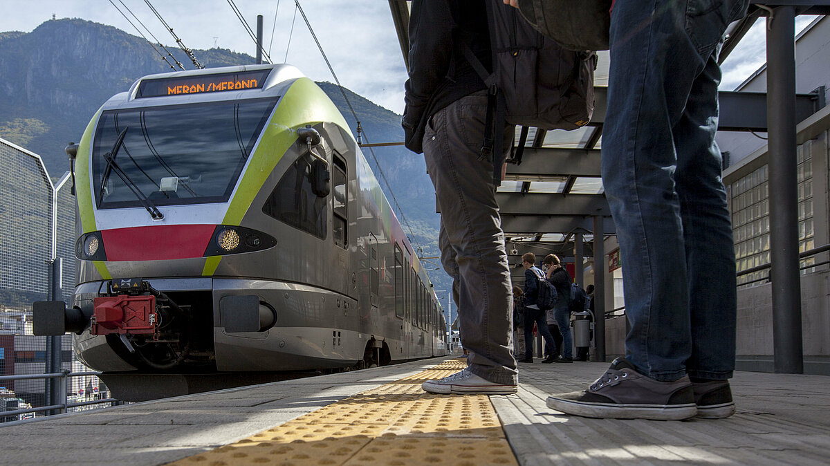 People and students waiting for the train at the station. The train is approaching